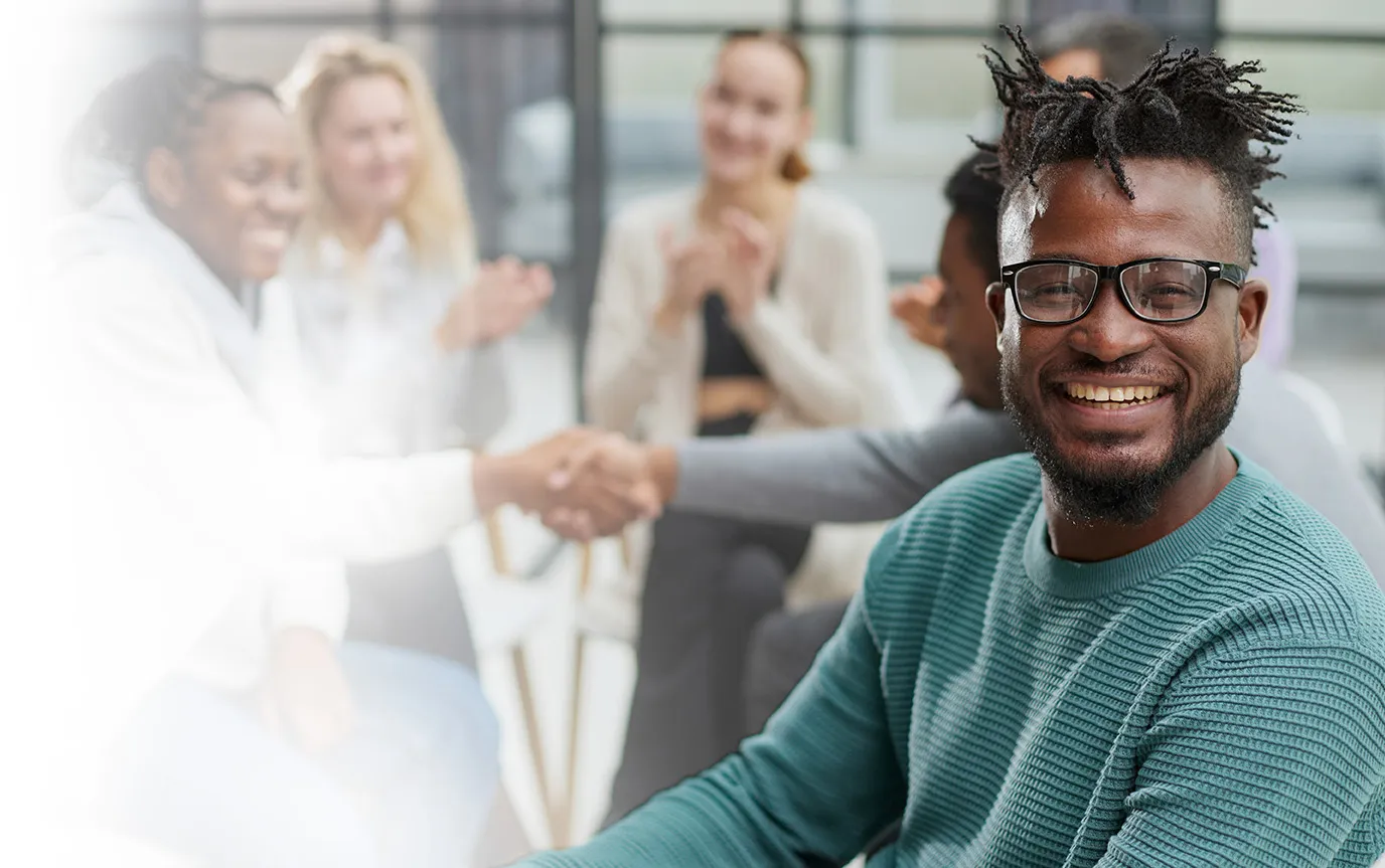 Image of man smiling with several people meeting in the background